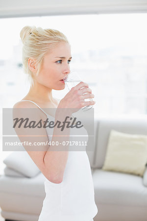 Side view of a fit young woman drinking water at the gym after working out