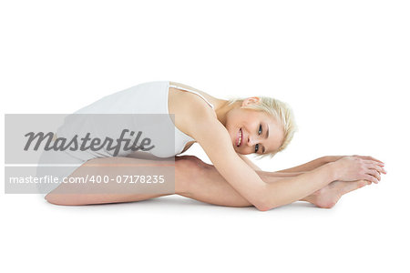 Full length side view of a toned young woman doing the paschimottanasana pose over white background