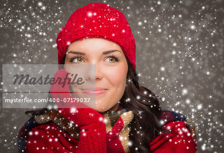 Happy Mixed Race Woman Wearing Winter Hat and Gloves Enjoys Watching the Snow Fall Looking to the Side on Gray Background.