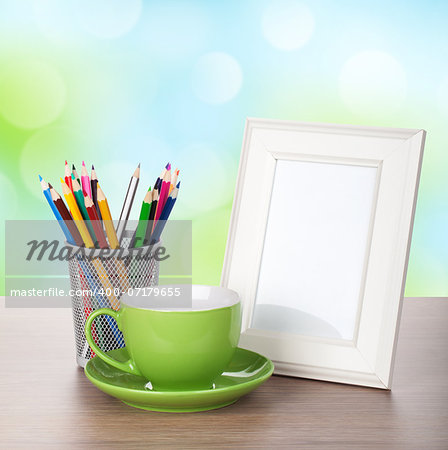 Photo frame, coffee cup and colorful pencils on wood table over sunny day bokeh background