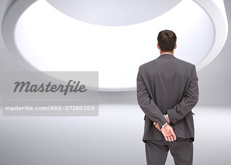 Composite image of businessman standing with hands behind back looking at huge circle in ceiling