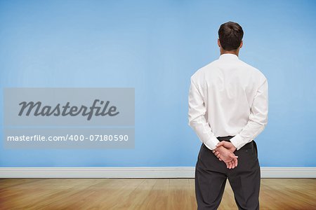 Composite image of businessman turning his back to camera looking at blue wall