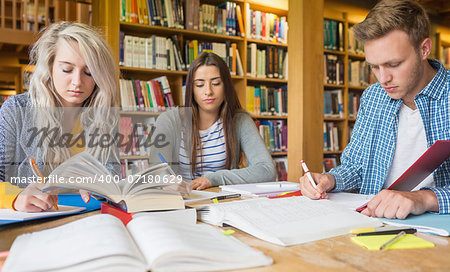 Group of three students writing notes at desk in the college library