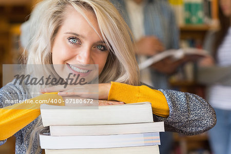 Close up of a smiling female student with stack of books while others in background at the college library