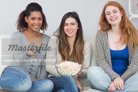 Portrait of young female friends with remote control and popcorn bowl on sofa at home