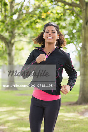 Portrait of a smiling healthy young woman in black jacket jogging in the park