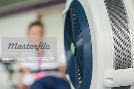 Determined young woman working out on row machine in fitness studio