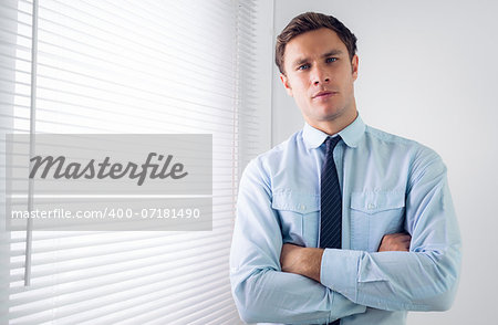 Portrait of an elegant young businessman standing with arms crossed in office