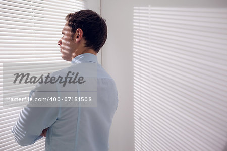 Rear view of a young businessman peeking through blinds in office