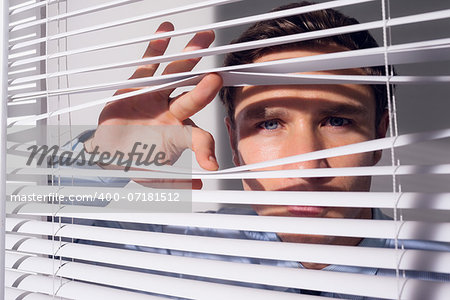 Close up portrait of a young businessman peeking through blinds