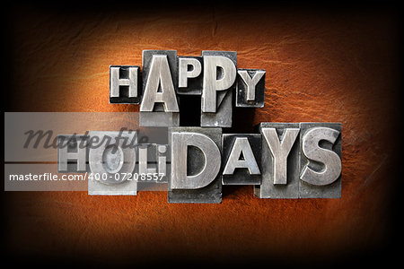 The words happy holidays made from vintage lead letterpress type on a leather background.
