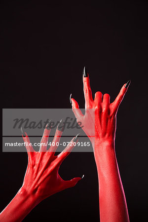 Red devil hands with long black nails, Halloween theme, studio shot on black background