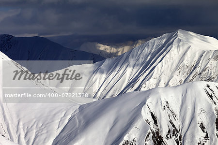 Snowy sunlit mountains and overcast sky. Caucasus Mountains, Georgia, view from ski resort Gudauri.