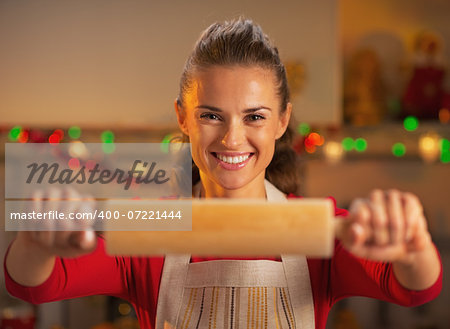 Smiling young housewife showing rolling pin