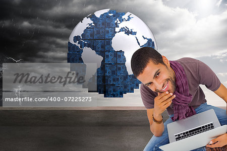 Composite image of thoughtful man sitting on floor using laptop and smiling at camera