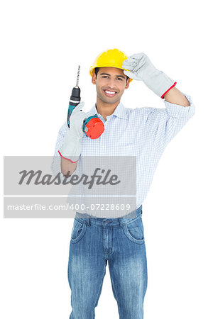 Portrait of a smiling handsome young handyman in hard had with drill standing against white background