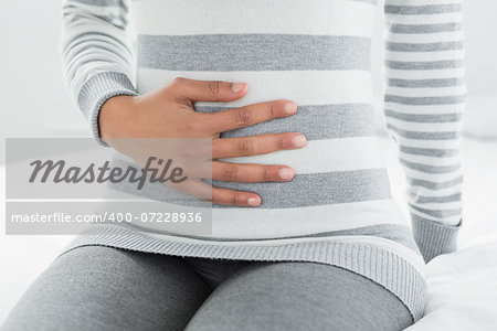 Close-up mid section of a casual young woman with stomach pain sitting in bed at home