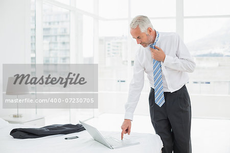 Side view of a mature businessman wearing tie while using laptop at a hotel room
