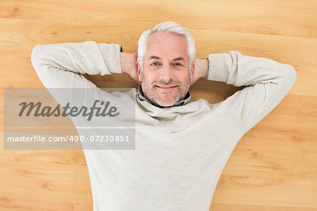 Overhead portrait of a smiling mature man lying on parquet floor at home