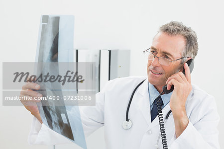 Male doctor looking at x-ray picture while using the telephone at medical office