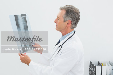 Concentrated male doctor looking at x-ray picture of spine in the medical office