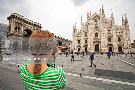 Young woman taking picture of Duomo di Milano (Milan Cathedral), Milan, Italy, motion blurred people on square