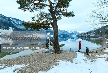 Cloudy winter Alpine  lake Grundlsee view (Austria) with fantastic pattern-reflection on water and family on shore.