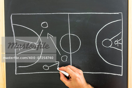 Closeup of basketball coach drawing game tactic on black board.