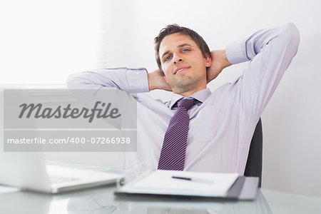 Portrait of a relaxed businessman sitting with hands behind head in a bright office