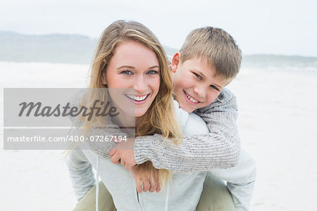 Portrait of a happy woman piggybacking her cheerful son at the beach