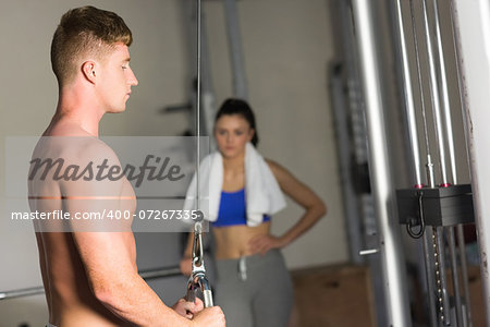 Young woman looking at determined sporty man use the lat machine in the gym