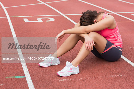 Full length of a tensed sporty woman sitting on the running track