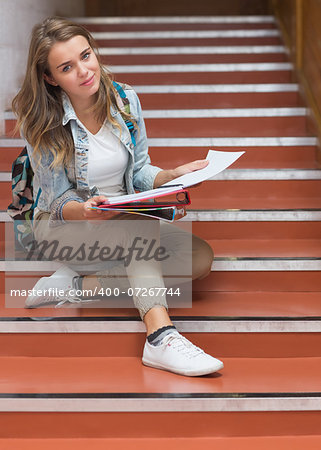 Happy young student sitting on stairs looking at camera in college