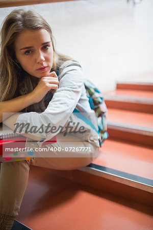 Troubled lonely student sitting on stairs looking at camera in college
