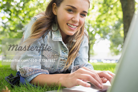 Young smiling student lying on the grass using laptop on college campus