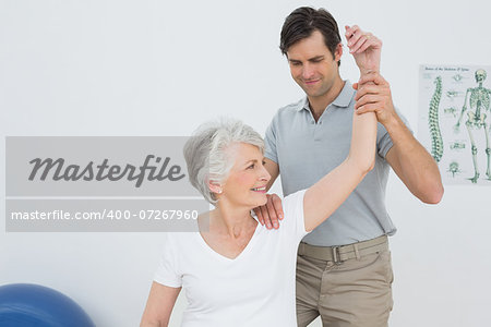 Male physiotherapist stretching a smiling senior woman's arm in the medical office