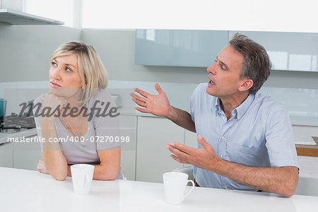 Casual couple with coffee cups having a fight in the kitchen at home