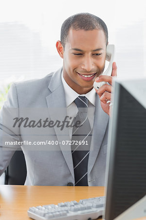 Smiling young businessman using computer and phone at office desk