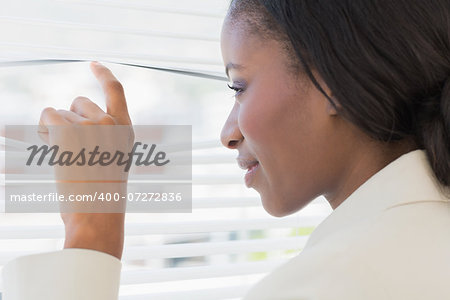 Closeup of a young businesswoman peeking through blinds in office