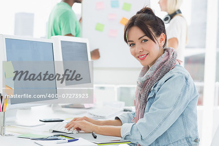 Side view portrait of an artist using computer with colleagues behind at the office