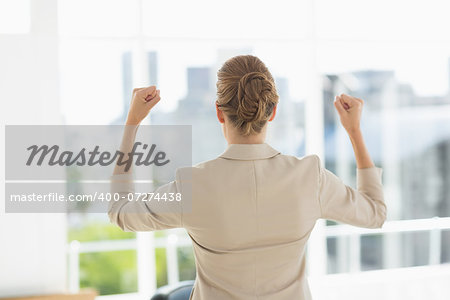 Rear of a cheerful young businesswoman clenching fists in a bright office