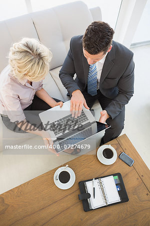 High angle view of a businessman and his secretary with laptop and diary sitting on sofa at home