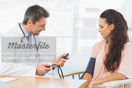 Male doctor checking blood pressure of a young woman at the medical office