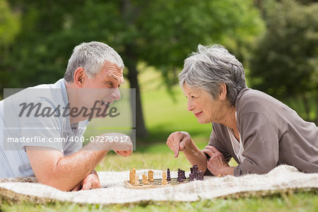 Side view of a happy senior couple playing chess at the park