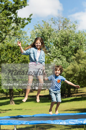 Full length of a happy boy and girl jumping high on trampoline in the park