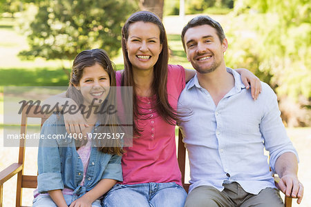 Portrait of a smiling couple with daughter sitting on park bench