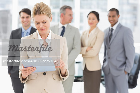 Businesswoman using her tablet with team behind her in the office