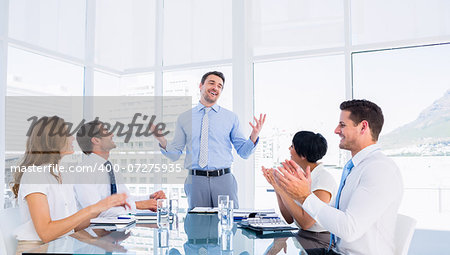 Business executives clapping around conference table in a bright office