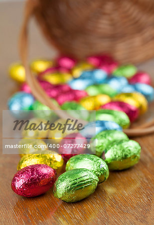 Colorful chocolate Easter eggs on the table and basket in background. Shallow dof