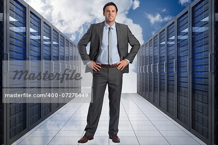 Smiling businessman with hands on hips against server hallway in the sky